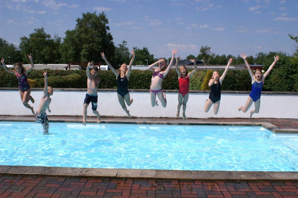 Børn hopper glade i swimmingpool en solskinsdag