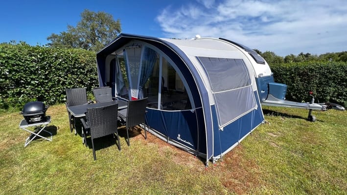 Campingvogn med fortelt og havemøbler på græsplads